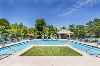 A large swimming pool surrounded by lawn chairs and trees.